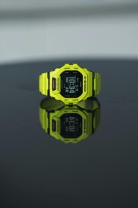 A vibrant yellow digital watch displayed on a glossy black surface, showing time clearly.